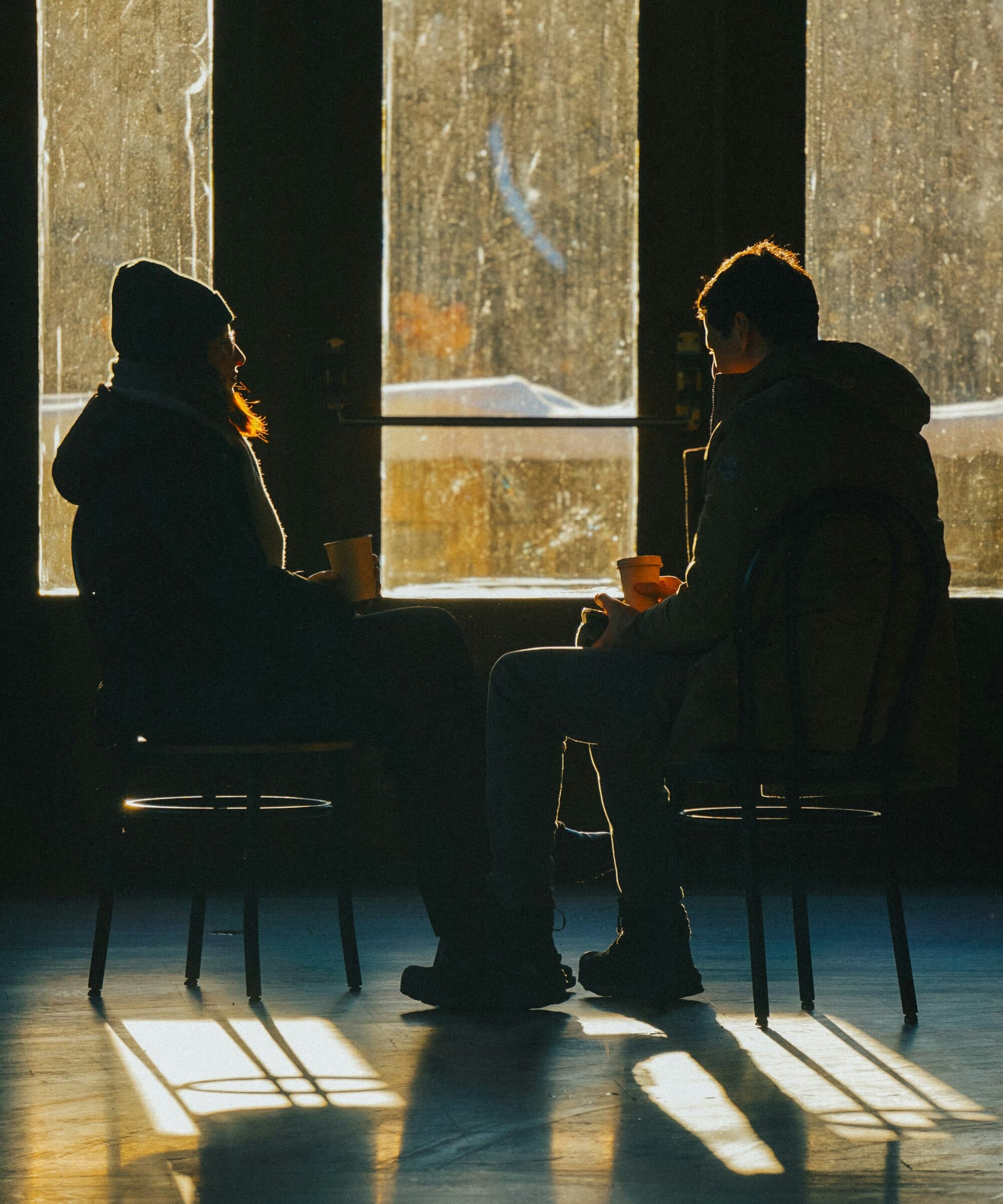 Dos personas conversan a contraluz junto a un ventanal