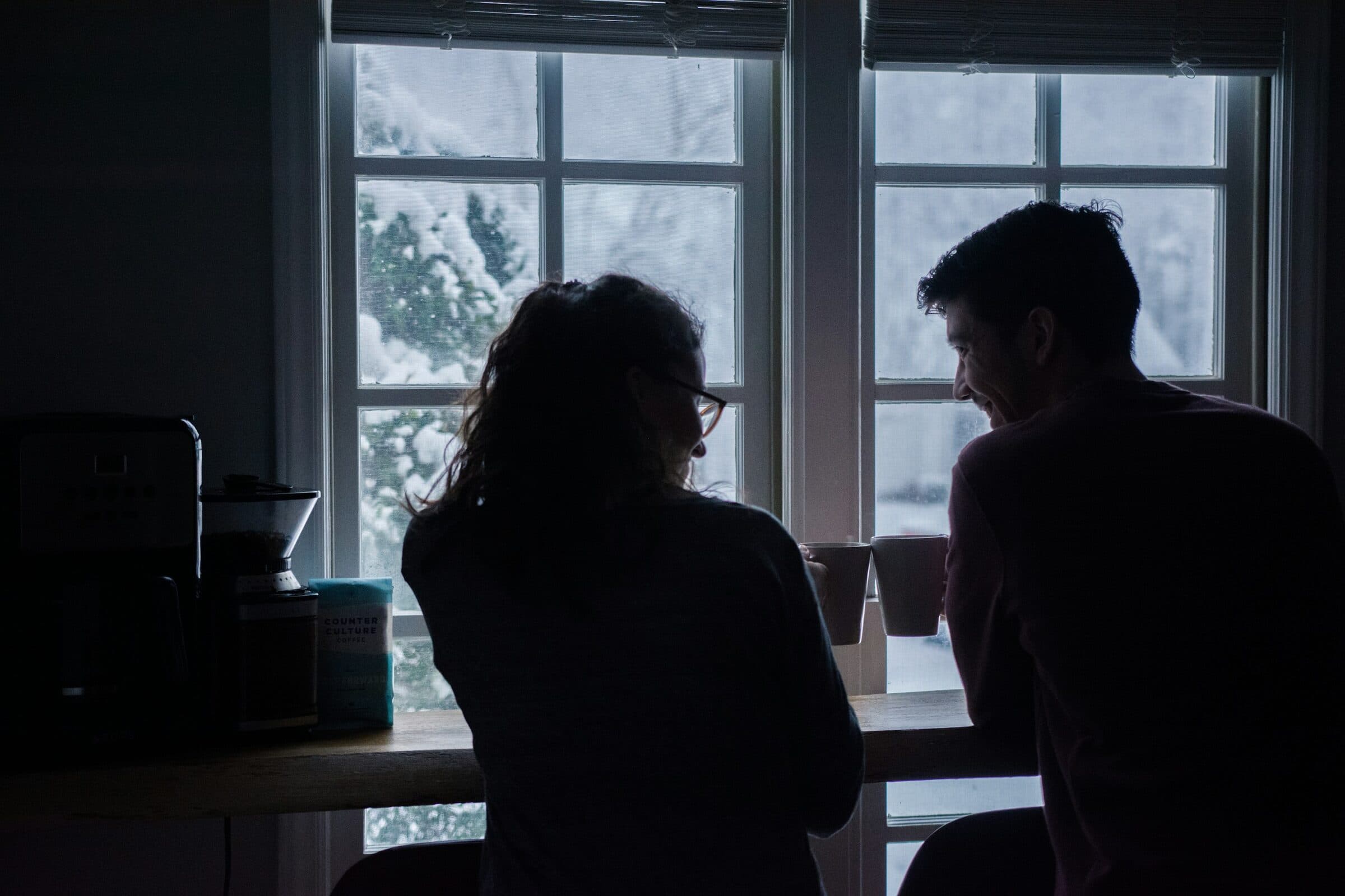 Una pareja charla de espaldas frente a una ventana nevada